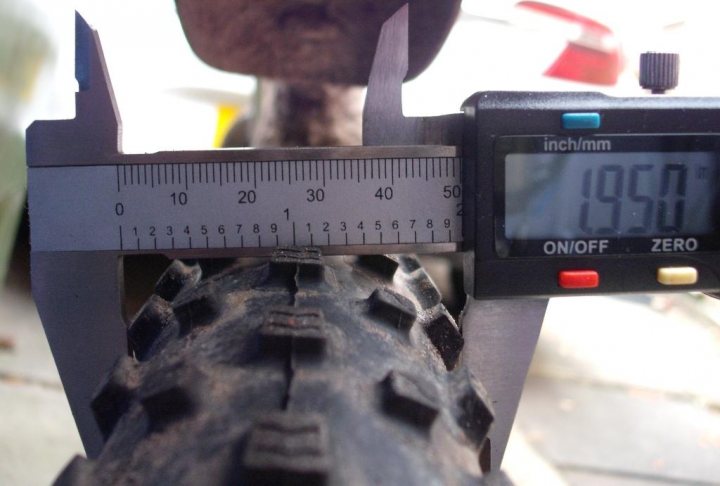 The "what bike bits have you just bought" thread - Page 312 - Pedal Powered - PistonHeads - This image features a measurement tool, which appears to be constructed of metal with adjustable nuts for fine tuning. The tool's base is housing a digital display and adjustment buttons. A scale strip with graduated markings is visible on the tool's surface. One end of the tool is pointing towards a tire, possibly being read by a device not visible in the image. In the background, there is a blurred human figure, possibly the person using the tool.