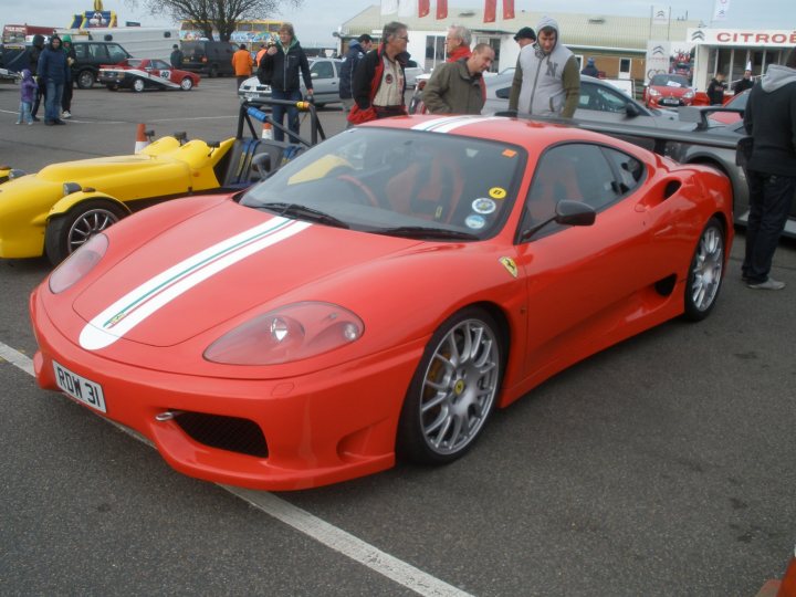 Thank you. - Page 1 - East Anglia - PistonHeads - This image captures a vibrant outdoor car show. The star of the scene is a sleek red Ferrari sports car. It is parked on a street with a yellow car in the background. The Ferrari is positioned in the foreground, drawing the viewer's attention. Around it, several people can be seen appreciating the car's design. In the background, there's a large building, suggesting that the show might be taking place in an urban environment.