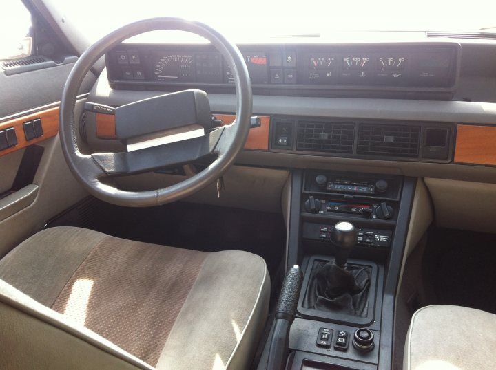 Pictures of my "NEW" SD1 Vitesse - Page 1 - Rover - PistonHeads - The image shows the interior of a vintage car featuring wood paneling on the dashboard. The steering wheel is arrangement in a semi-circular fashion, surrounded by several buttons and dials, indicative of the car's early electronic amenities. In the foreground, you can see the front seats and the center console, covered in a fabric that appears to be rippling, which suggests a warm environment or perhaps sunlight streaming through the car's windows.