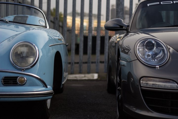 The GT Cafe - the ace cafe of the north - Oct Meet - Page 1 - North West - PistonHeads - The image depicts a striking scene on a dimly lit street. Dominating the scene are two iconic cars, rendered in a moody grayscale color palette. A vintage blue Porsche 356, characterized by its round headlights and timeless design, is parked on the left. Its metallic blue hue stands out against the gloomy backdrop. On the right, a sleek black Porsche Cayenne, featuring razor-sharp headlights and a sleek silhouette, is parked. Despite being in color due to the studio setting, it mirrors the same vintage aesthetic.