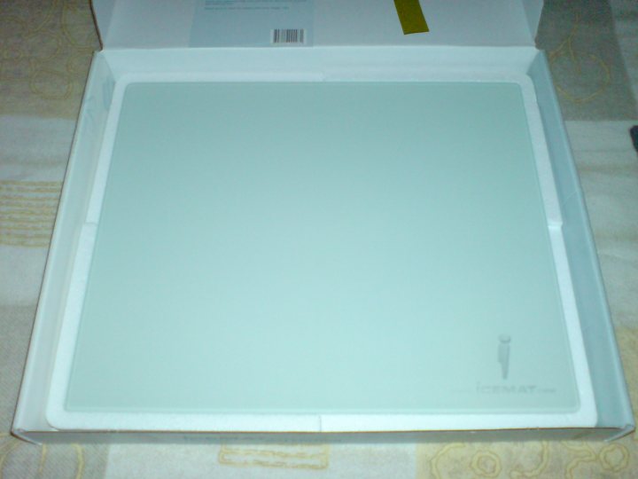 The image shows a flat white package open, revealing a clear plastic base with a blank space that has been sanitized. The interior of the package is white and boxed, and the overhead pictures of what is in the package aren't clearly visible. There are labeled packing instructions at the back of the package, along with some small text which appears to be a barcode. It's a new product, as indicated by the packaging.