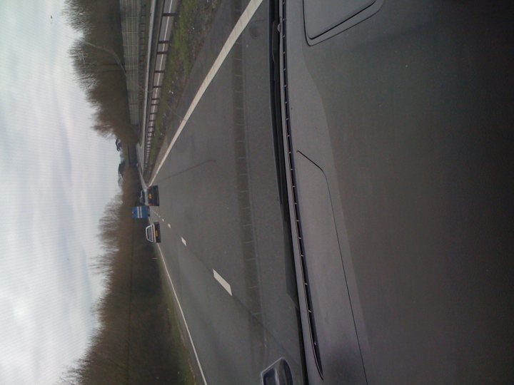 What is the trend? - Page 1 - Honda - PistonHeads - The image presents a view from inside a car, showing a stretch of highway bordered on the right by a barrier. On the opposite side of the barrier, there appears to be a line of vehicles including a lead car. The highway is flanked by what looks like trees or bushes, indicating that the route is potentially rural or semi-rural. The image is slightly distorted, likely affecting the visibility of the cars in the coming traffic due to the reflection in the windshield.