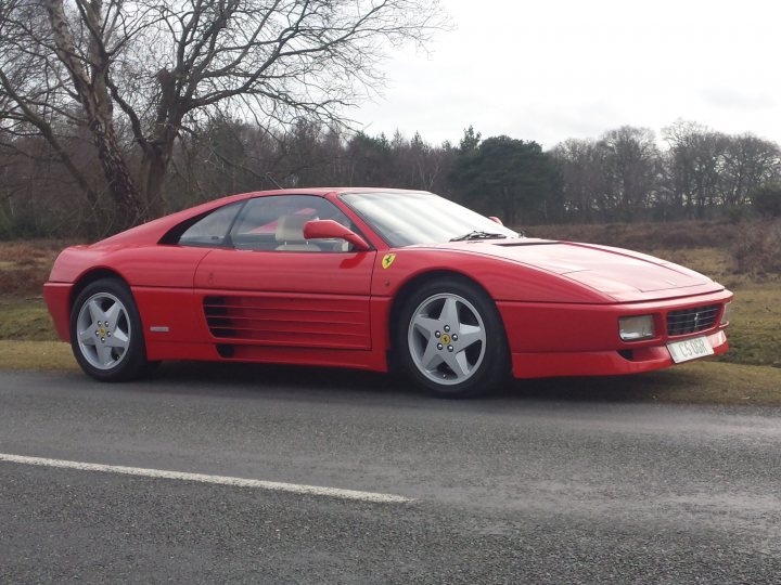 Ferrari 348 buying advice please - Page 1 - Ferrari V8 - PistonHeads - The image depicts a red Ferrari convertible resting peacefully on a rural road, surrounded by a backdrop of trees. The sleek car is parked on the side of the road, its convertible top open, revealing a vacant passenger seat. The surrounding greenery suggests a serene, almost secluded location. The car appears to be a Ferrari, a make known for its prestige and performance, hinting at the rich and dynamic lifestyle of its owner.