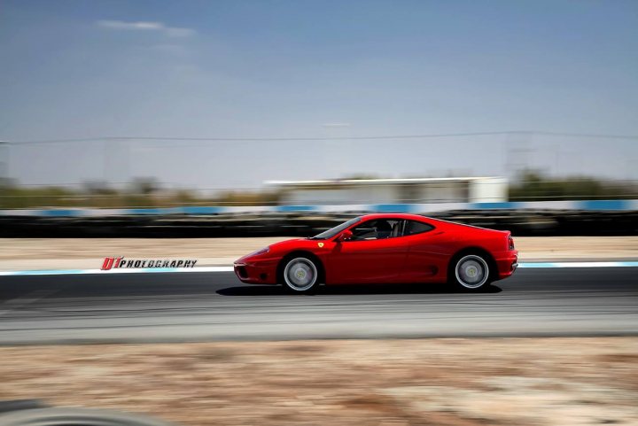 Ferrari track action in CYPRUS - Page 1 - Ferrari V8 - PistonHeads - The image captures a vibrant red sports car racing on a track. The sports car, positioned in the center of the frame, is moving at a high speed, conveying the sense of speed and intensity. The blurred motion lines suggest the vehicle is in action, creating a dynamic and thrilling scene. In the background, one can spot other cars on the track, indicating an ongoing race event. The overall setting is open and clear, emphasizing the focus on the speeding car.