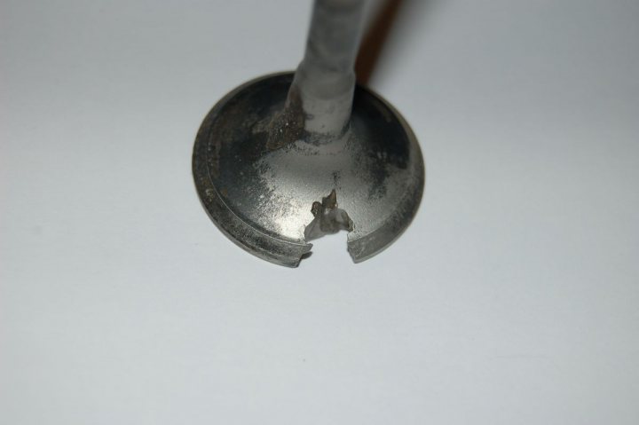 What made this valve fail? - Page 1 - Home Mechanics - PistonHeads - The image shows a close-up view of a chipped metal surface. A spoon, which appears worn and damaged, is prominently featured, with a large chip in its handle area. The spoon rests on a stark white background. The close-up perspective allows for a detailed examination of the spoon's condition, emphasizing the jagged edge of the chip and the remaining, smooth metallic surface. The color contrast between the gray of the spoon and the white of the background further highlights the spoon's condition.