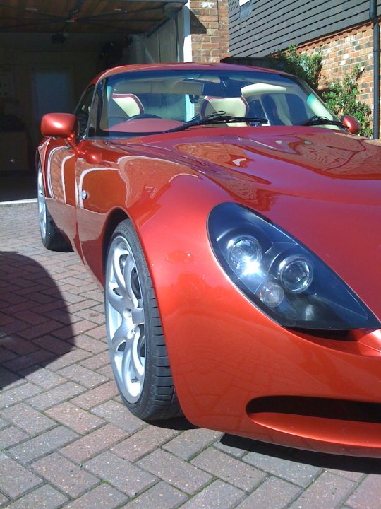 Pistonheads - The image captures a scene featuring a striking red sports car parked on a cobblestone driveway. The car, which is the main focus of the image, is painted a glossy metallic red that gleams against the bricked pavement. Its sleek design and elongated hood are indicative of a high-performance model. A black frame lines the top of the windshield, adding a touch of contrast to the overall red color theme. The car is angled slightly to the left of the frame, giving the viewer a clear view of its profile. In the distance, partially obscured by the side of the car, there is a door leading to an area with a white wall, suggesting that the photo was taken in a residential or park-like setting.