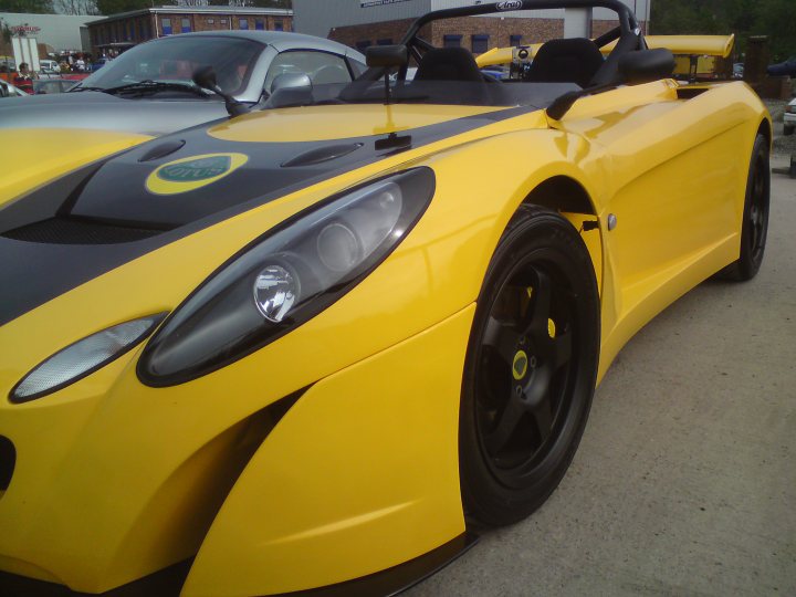 Pistonheads - In the image, there is a striking black and yellow sports car parked on the side of a road. Its design is sleek and aerodynamic, indicative of a fast and powerful vehicle. The car appears to be the centerpiece of the photo, with a backdrop of an overcast sky and a tree-lined street. There are also a few other cars in the background, providing context for the location. The overall composition of the image suggests it might be part of a car show or exhibition.