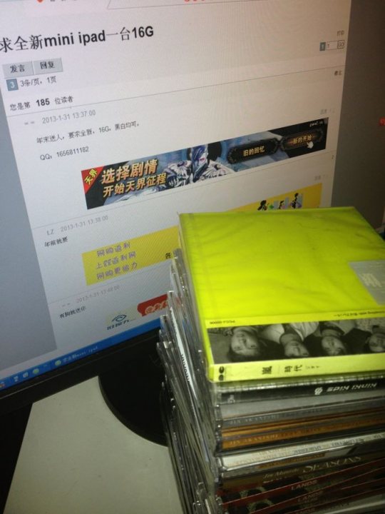 The image shows a computer screen with Chinese text on it, which appears to be an online purchase order for an Apple iPad model number 16G. The text on the screen mentions the date of April 18th, 2014, and possibly some details about the purchase. Below the screen, there is a stack of compact discs. The primary disc is a yellow CD, and below it are a number of other music CDs in various colors. The setting suggests someone who is interested in music and possibly organizing or sorting through their CD collection in front of their computer.