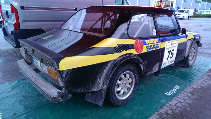 SAAB 99T rallycar pics - Page 1 - Saab - PistonHeads - The image shows a small, black and yellow sports car parked on a wet surface, likely a parking lot. There is writing on the car, including "TORI SAB" and "75," along with other smaller details. The vehicle appears to be in good condition, with no visible damage or wear. The car is parked next to a purple vehicle during the day.