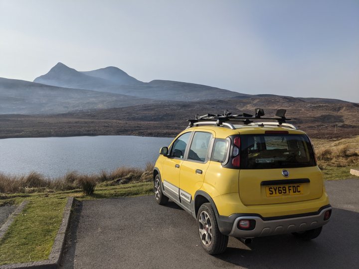 The Retina Burner - Panda Cross 4x4 Content - Page 1 - Readers' Cars - PistonHeads UK - The image shows a vibrant yellow SUV parked in front of a serene lake with mountains rising majestically in the background. The vehicle is equipped with bicycles on its roof, suggesting an active outdoor lifestyle or trip. The sky above is a clear blue, and the overall setting appears to be a calm and picturesque day in a mountainous area.