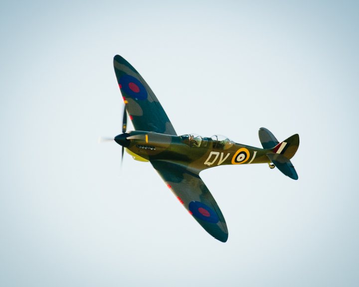 Revival images - Friday  - Page 1 - Goodwood Events - PistonHeads - The image showcases a vintage propeller fighter plane in flight against a clear blue sky. The plane exhibits a combination of dark green and red camouflage paint, with unusual technical designations in white on its wings and body. The wings are adorned with red, white, and black rings, likely signifying national insignia. The airplane is angled slightly downward, with its nose pointing forward, giving a sense of motion and combat readiness. The photograph conveys a vivid sense of nostalgia for the aviation history of the 20th century.