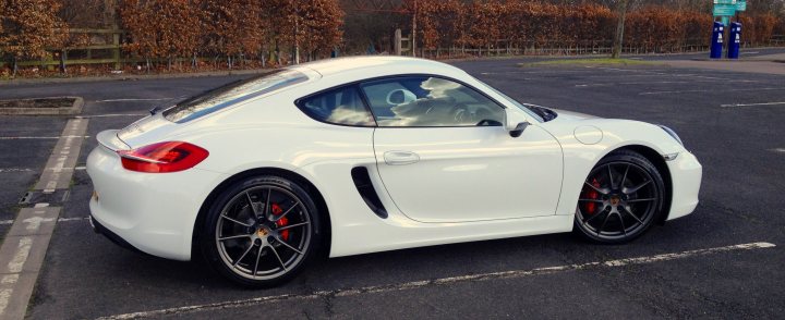 Boxster & Cayman Picture Thread - Page 8 - Boxster/Cayman - PistonHeads - The image presents a scene featuring a white Porsche sports car parked in a parking lot. The car's sleek design is accentuated by the contrast of the white body with the black paint on the bottom. It is outfitted with black wheels on the side and a red stripe running along the roof, highlighting the car's sporty nature. The vehicle is parked perpendicular to a white line in the parking lot, with a clear view visible through its front window. There is also a hint of pumpkins and dark-colored shrubbery in the background, suggesting an early autumn setting.