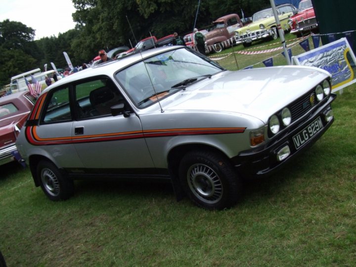 A white truck parked in a parking lot - Pistonheads - This image displays a vintage car, specifically a silver four-door, parked on grass at an outdoor show or exhibition. The car features distinctive orange and black stripes running along the side, a typical design characteristic of certain eras in automobile history. The wheel arches and hubcaps indicate the era of the vehicle as well. Despite the car being the focal point, the background is crowded with other cars, suggesting a larger event with multiple vehicles on display, possibly even a car show. The setting seems to be a sunny day, as indicated by the shadows cast by the cars and the act that the car seems to be in the shade, possibly under someone's umbrella.