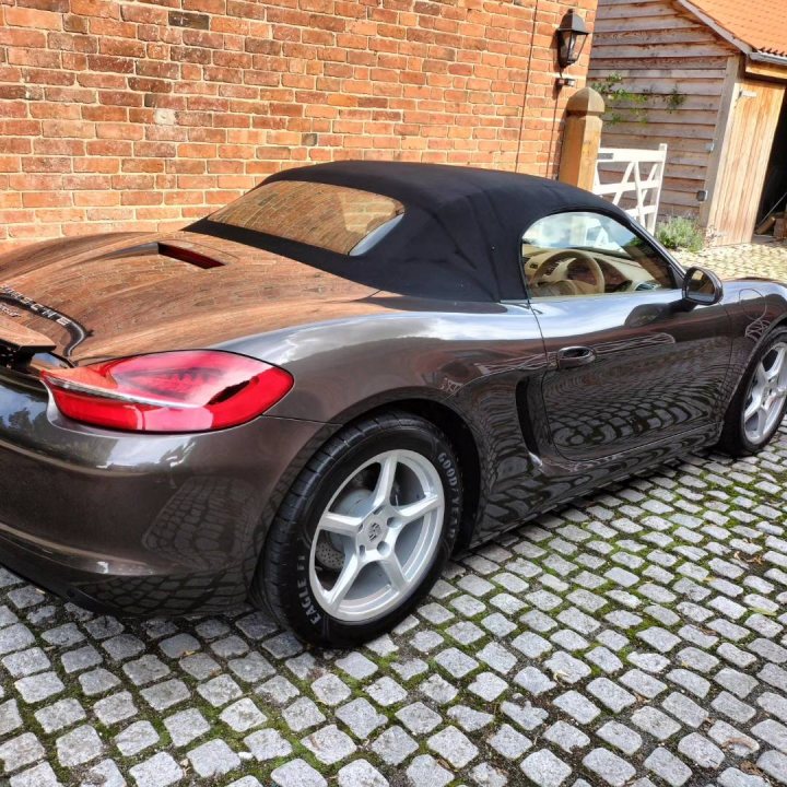 Pistonheads - The image features a dark-colored sports car parked on a cobblestone driveway. It appears to be a sunny day, as indicated by the shadows cast by the vehicle and objects around it. The car is equipped with a convertible top that is partially open, revealing the interior. There are no visible passengers in the car, suggesting it may be unoccupied at the moment. The car's design, including its aerodynamic body and sporty wheels, indicates it is designed for high-performance driving.