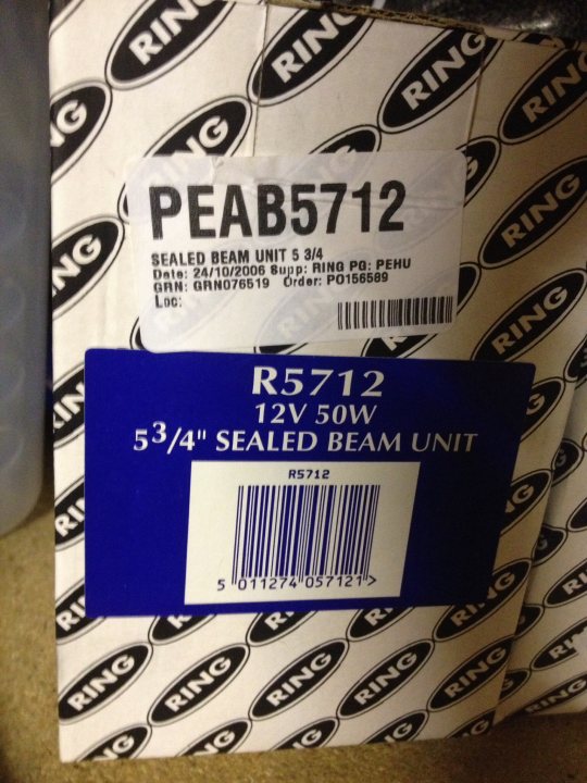 2.5 headlights what are they off ? - Page 1 - Noble - PistonHeads - This image shows a strategic placement of two product tags within a white background, possibly within a packaging material. The upper tag reads "PEABS57112" and provides details about a "Sealed Beam Unit" from "RING". The lower tag is also from "RING" and reads "R5712" with "BEAM UNIT" printed on it, indicating that these items are related to a beam unit manufactured by RING for a product code PEABS57112. The tags also include serial numbers and a QR code, which are commonly used for inventory and tracking purposes.