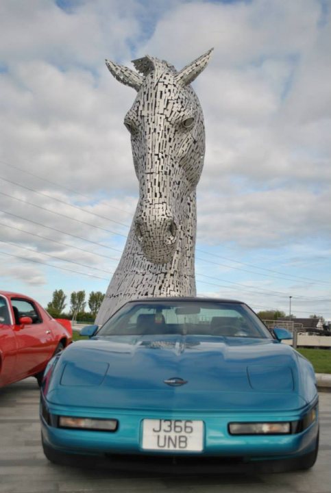 Pistonheads - The image shows a vibrant and modern scene featuring a sports car and a prominent, metallic sculpture of a horse's head. The horse's head sculpture is large and primarily white, composed of small tiles that together form the contours of the horse's face. This art piece is situated outdoors next to a blue sports car that has a sleek and rounded design. The sky is partly cloudy, suggesting a breezy day, and the overall setting appears to be a public art display or an auto show meeting European standards.