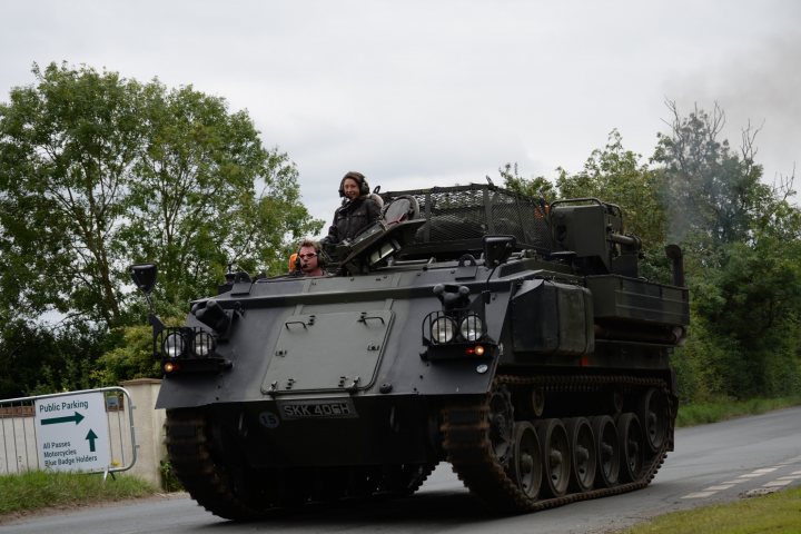 Spotted 2017 - Page 13 - North East - PistonHeads - The image depicts a military scene with an armored personnel carrier (APC) parked on the side of a road. There are at least two individuals visible, inside the vehicle, one of whom appears to be the driver. The APC is a heavy-duty military vehicle, designed for transporting troops and equipment, equipped with a turret on top. The setting seems to be an open country road with trees and shrubs lining the sides. There is a sign near the APC, possibly indicative of a restricted area, but the content of the sign is not clear.