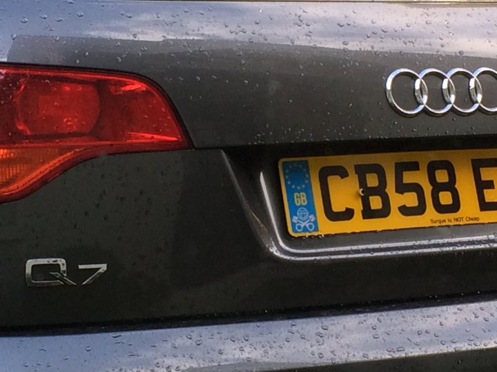 Q7 4.2 TDI - owner reviews and tips sought - Page 1 - Audi, VW, Seat & Skoda - PistonHeads - The image features a close-up view of the rear license plate area on a vehicle. The license plate is prominently displayed, reading "CB58 F". The car's model, "Q7", can be seen to its left. The vehicle has a distinct design with a prominent corporate logo centered on the trunk lid. The trunk area appears to be wet, suggesting recent rain, and there are droplets scattered across the camera lens, suggesting the photo may have been taken shortly after the rainfall.