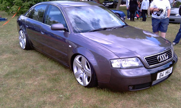 Cars On The Green - Photo Thread - Page 1 - East Anglia - PistonHeads - The image depicts a luxurious purple Audi car prominently displayed on a lush green grass field. The car is viewed from its rear side, showcasing its black roof and black alloy wheels. The setting appears to be a car show or an outdoor exhibition, as evidenced by the presence of several other cars and people in the background, suggesting a social event. The license plate of the Audi reads "B4 HONE 6W," indicating it might be a show car with distinctive modifications and custom features.