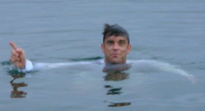 Any Take That fans? - Page 1 - Music - PistonHeads - The image is a candid photograph featuring a person partially submerged in water. The individual, who appears to be a young man with a neutral expression, is reaching out with one hand. His body is oriented towards the camera but his head is turned to the side, away from the lens. The background is out of focus, emphasizing the subject in the center of the frame. The lighting suggests it could be evening, and the water appears calm.