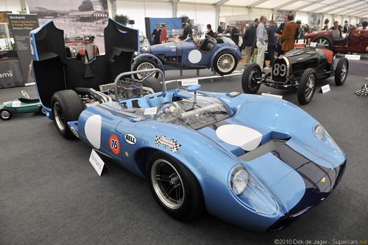 Pistonheads Douglas Gardner - This image captures a display at a car show featuring classic race cars. Three distinctive models are showcased in a spacious indoor arena. The first is a blue race car with an open door, revealing its curved and polished design. Next to it, a green race car is slightly larger, hinting at its power and speed. The third race car is a black racer with a visible number, contributing to the competitive atmosphere of the event. The display includes spectators, immersing the scene in the excitement of a car race with cars on full display for all to admire.