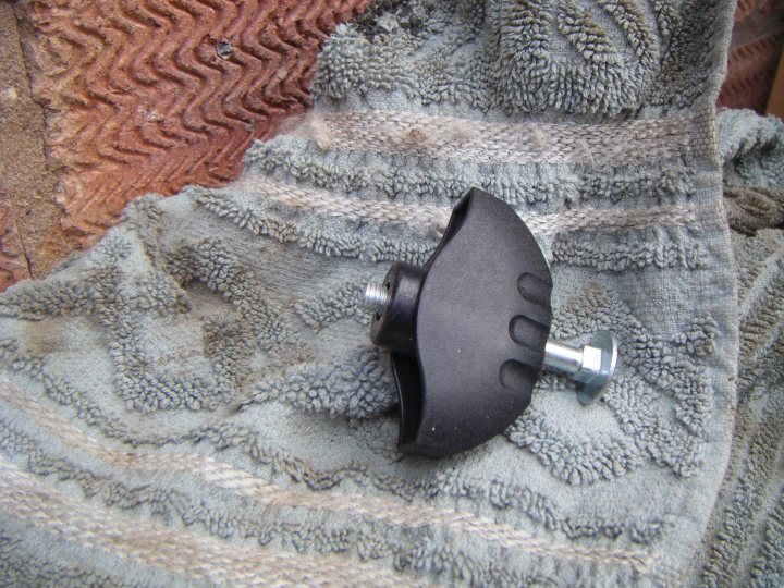 Fuel Filler Cap Security Idea - Page 1 - S Series - PistonHeads - The image shows a black plastic case lying on a textured, multi-colored fabric. The textile appears to be well-used, with distinct patterns and shades of red, beige, and gray. The one visible tool is a metallic object with a round, hole-like form at one end and a cylindrical shape with multiple patterns at the other. The metallic object seems to be possibly a lens attachment or a light fixture attachment for a vacuum cleaner.