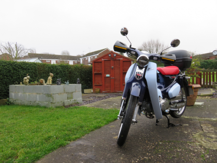 A picture a day....biker banter (Vol 5) - Page 291 - Biker Banter - PistonHeads - The image depicts a scene in a residential area. A blue and white motorcycle is parked on the side of a road. The motorcycle is leaning slightly, indicating it has been recently parked or is about to be moved. It's parked next to a neatly kept garden with a green lawn and some decorative elements. In the background, there are houses visible, suggesting this scene takes place in a residential neighborhood.