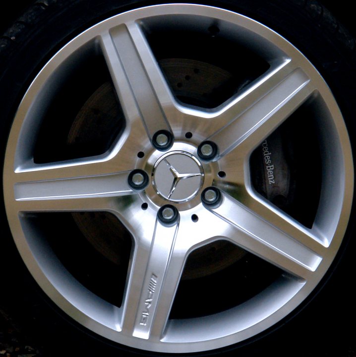 Pistonheads - The image provides a close-up view of a car's silver alloy wheel. The wheel has a spoke-style design with rounded ridges and a hub in the center featuring the logo of the manufacturer. The spokes extend outwards to the hub, creating a rhythmic pattern for the wheel's structure. The image itself showcases the wheel's metallic sheen, suggesting it's clean and well-maintained. The hubcap is visible, indicating the wheel might be a Mercedes-Benz aftermarket or custom choice. The image is cropped to focus solely on the wheel and its details.