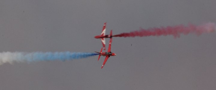 Four airplanes flying in formation in the sky - Pistonheads - The image captures a breathtaking scene of an airshow, where two fighter jets are executing a precision trick. The jets, painted in a vibrant combination of red and white, are flying side by side, leaving behind contrails of red and blue smoke. The birds-eye perspective from below emphasizes the skill and precision of the pilots. They are flying tightly, showing their mastery and synchrony.