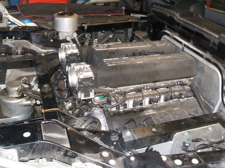 Pistonheads - The image shows the engine bay of a vehicle. The focus is on the complex system of wires and components that make up a car engine. Several engine parts are visible, such as pipes, filters, and metal housings for various components. Some of the parts are black, and there are signs of wear or grease, indicating that this might be a mechanical or technical service setting. The engine seems to be under the hood of a vehicle that is in a state of construction or repair.