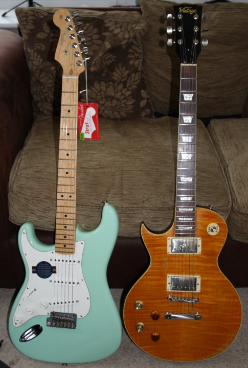 Lets look at our guitars thread. - Page 49 - Music - PistonHeads - The image shows two electric guitars against a background featuring a sofa with a floral pattern. The guitar on the left is a light blue, with a shaping resembling a Stratocaster. The guitar on the right is an orange, with a design that resembles a Gibson L-shaped guitar, possibly a Gibson Les Paul. Both guitars appear to be acoustic or semi-acoustic, as indicated by their pickguards and the unplugged state of the pickups. At the bottom of each guitar's body, there are control knobs suggesting they have pickup and background noise controls.