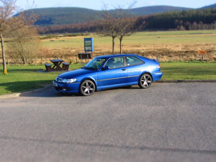 Pistonheads - The image captures a serene scene in a country setting. A blue car is parked on the side of a road, adjacent to a grassy field that stretches into the distance. The car's vibrant color stands out, suggesting it's a sunny day with good visibility. In the background, the calm vastness of the field is dotted with trees, indicating that the car is in a rural area. A wooden bench can be spotted off in the distance, possibly for visitors to sit and enjoy the peaceful scenery.