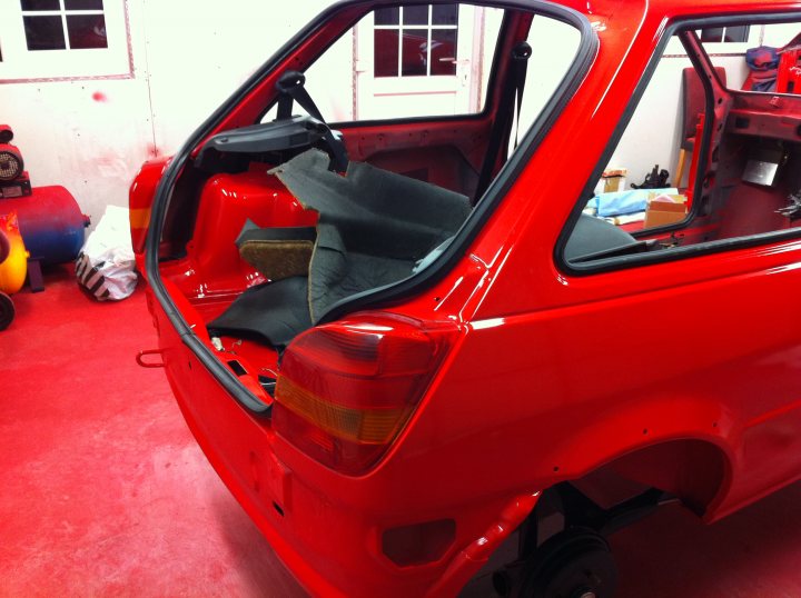 Pistonheads - The image captures the interior of a red car, viewed from the side rear reaching deep into its interior towards the top left corner. The car's seats are in a state of disarray, with several items strewn inside. The back windshield is visible, offering a perspective of the interior that also includes the front seats. The floors of the car are not visible, and the focus remains on the interior space and seats. The sides of the car are discernible, with the body and surface texture suggesting a level of shine, possibly following a thorough cleaning or preparation for painting.