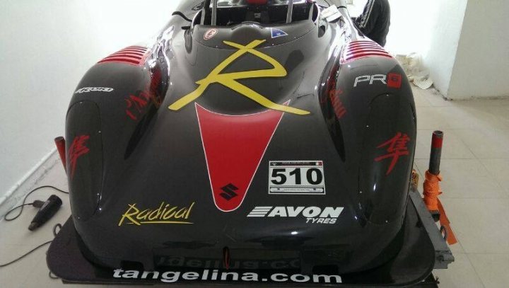 Weight of carbon wing - Page 1 - Radical - PistonHeads - The image features a black racing car with vibrant red and yellow accents, prominently displaying a large "R" emblem in the center. The front of the car is adorned with the Avon logo, and it bears the number "510", likely representing its racing classification or identification. The car appears to be new or well-maintained, suggesting that it might be used in professional racing events. In the background, a smaller figure of a person is barely visible, possibly indicating the presence of someone near the vehicle.