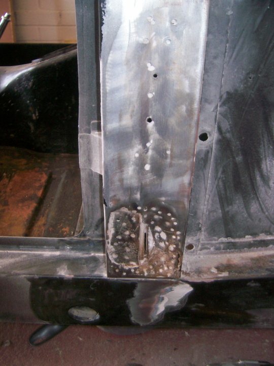 Pistonheads - The image shows a close-up view of a car's metal engine cover with a pattern of bumps or studs on its surface. The cover appears to be used and possibly rusty in some areas, especially at the corners where it attaches to the vehicle body. There are visible spots where the paint has worn away, exposing the underlying metal to corrosion. Traces of machining or smoothing can be seen around some of the studs, indicating maintenance or repair work might have been performed. The backdrop is blurred but suggests a garage or workshop environment.