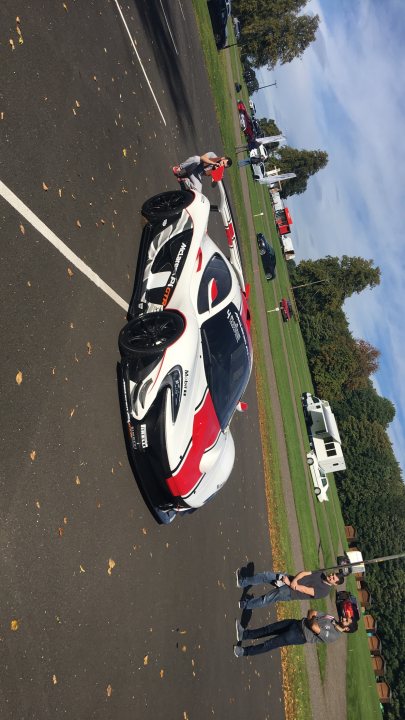 Spotted 2017 - Page 10 - North East - PistonHeads - The image captures a vibrant scene at a car show. At the center of attention is a striking white and red sports car, parked on a concrete lot. The car boasts an eye-catching design with a large rear wing and sleek lines, indicative of its high-speed capabilities. The lot is populated with other cars and trailers, suggesting other exhibitors in the field, but the sports car undoubtedly steals the show. In the background, a lone figure can be spotted, possibly a passerby or an attendee. The overall atmosphere is that of excitement and anticipation, as car enthusiasts gather to admire the latest models.