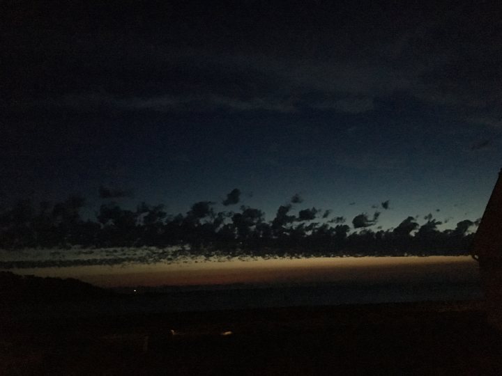 The 2017 summer and thunder thread - Page 29 - The Lounge - PistonHeads - The image captures a serene night scene at what appears to be the ocean. The sky is dark, providing a stark contrast to the colorful cloud formation that stretches across the horizon. The clouds are a mix of various shades, leaning towards hues of orange and pink, which are likely the result of the sunset. Beneath the dramatic skyline, the calm sea surface is barely visible, indicating the time is likely early evening. From this perspective, the clouds are seen as a silhouette against the dark, ominous sky. It's a powerful and scenic view that conveys a sense of tranquility and the end of another day.