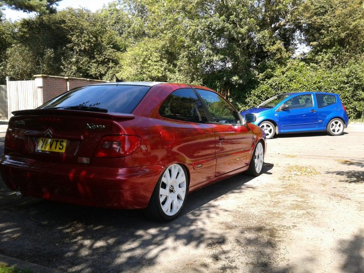 My Two French beauties. - Page 1 - French Bred - PistonHeads - The image showcases a serene parking lot scene, featuring two parked cars. The red car is parked closer to the foreground, while the blue car is parked further back. Both cars are positioned in front of a fence and under the shade of trees, making for a peaceful atmosphere. The red car is a compact car, as indicated by its size in the image, while the blue car appears to be a larger model. The number "175" is visible on the red car's license plate.