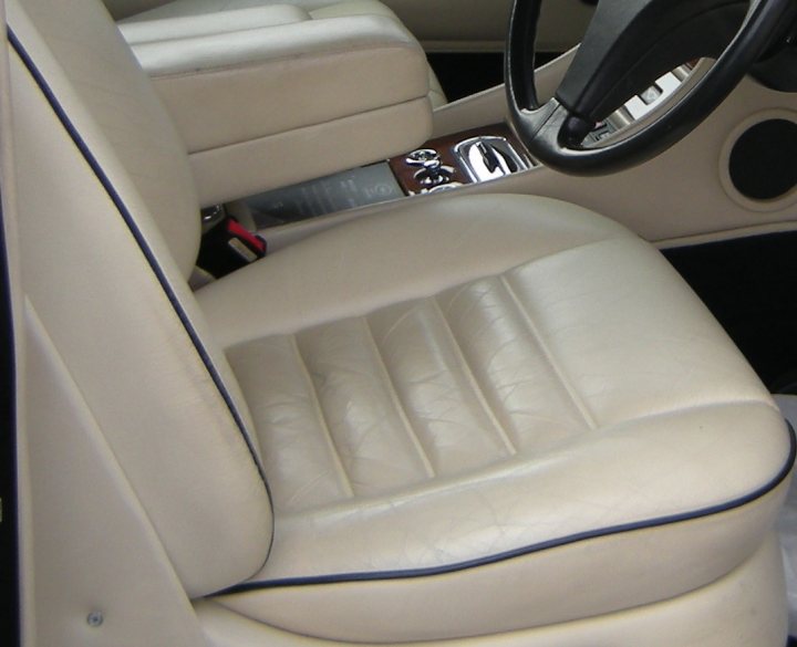 Leather seat cleaning suggestions please - Page 1 - Rolls Royce & Bentley - PistonHeads - The image shows the interior of a car's front seat. The seat appears to be upholstered in a creamy beige fabric, with a visible texture across the seat surface. The headrest is attached to the back of the seat, providing a safe position for drivers and passengers. To one side, the door frame is partially visible, indicating that the seat is situated next to the car's door. There are no passengers sitting on the seat, and there are no distinct objects or clutter on the seat. The bottom of the steering wheel is not fully visible, but it seems to be part of the car's safety belt system. Overall, the image gives a sense of a clean, tidy vehicle interior.