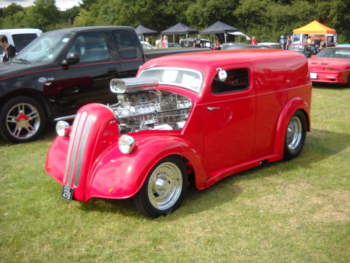 Anyone going to the NASC 40th Nats at Trinity Park? - Page 1 - East Anglia - PistonHeads - The image showcases a vintage red and silver tow truck in the foreground, parked on a grassy area. The truck is facing the viewer, revealing a partially opened engine hood. In the background, there are other classic vehicles, including a black pickup truck and a classic red car, suggesting that this might be a car show or a gathering of vintage vehicles. Among the vehicles, several people can be spotted, possibly attendees or owners of the cars. The atmosphere appears to be outdoors during daylight.