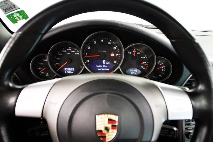 Porsche 997 911 Carrera - Page 1 - Readers' Cars - PistonHeads - The image captures the interior of a car from the perspective of the driver's seat. The steering wheel is prominently displayed in the foreground, with black and silver panels. Behind it, the car's dashboard is visible, showing several gauges and indicators. In the middle of the dashboard, there is a radio display screen. The image is taken from a high angle, giving a broad view of the car's steering wheel and dashboard. The digital elements, such as the radio display screen, suggest a modern car.