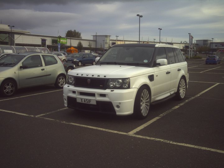 Scotland's Finest Spotted!! [Vol 2] - Page 8 - Scotland - PistonHeads - In the image, a parking lot is filled with several cars. The focus is on a white Range Rover with the registration "X ASI" on the left side. This SUV is parked alongside a row of other vehicles. The background reveals the outlines of buildings under a cloudy sky.