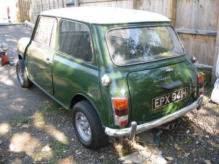 Pistonheads - The image features a vintage, green Toyota Corona works car parked on a gravel driveway with patches of grass and a wooden fence in the background. The car, with its distinctive round headlights and badge on the side, appears to be well-used and is the central focus of the photograph. The weather appears to be partly cloudy, and there is a clear road in the background. The cars design suggests it might be from the 1960s, known as a works car, typically used by mechanics or workers associated with the car company.