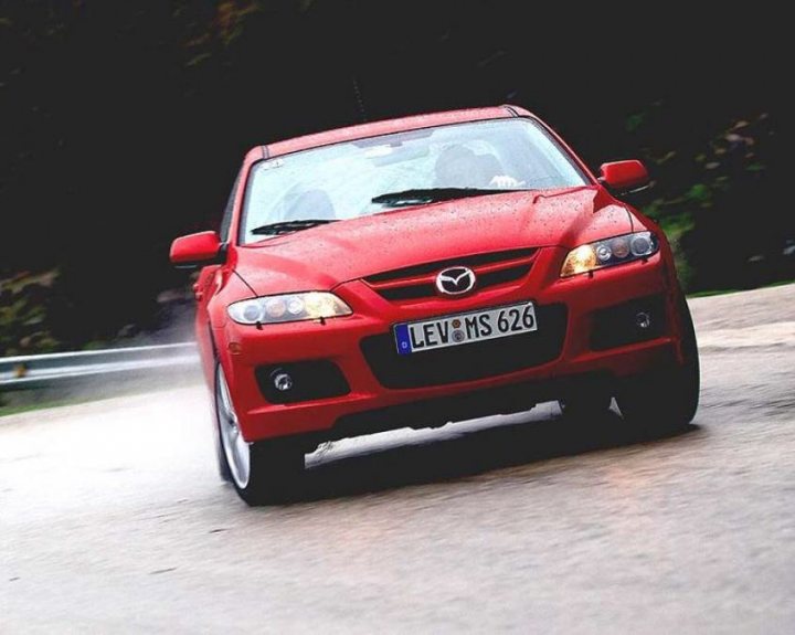 Uber - Page 1 - Australia - PistonHeads - The image is a dynamic photograph of a red Mazda Levens 260, which suggests it's a European version given the license plate format. The car is in motion, as implied by the slight blurring on its wheels and the water droplets captured in the air. The road appears to be a bit wet, possibly after rain, contributing to the car's dynamic trajectory across the frame. The style of the photo conveys a sense of speed and the motion of the car, with the in-motion effect adding a visual impact to the scene.