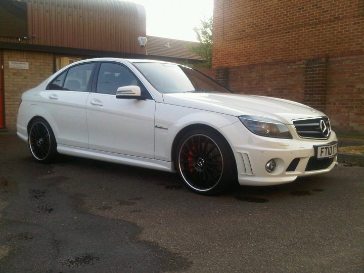 Show us your Mercedes! - Page 9 - Mercedes - PistonHeads - The image depicts a white Mercedes-Benz parked on a street next to a red brick building. It's an up-close photo focusing on the car's side profile. The Mercedes vehicle features a sleek design with a set of two exhaust pipes at the rear. The vehicle is equipped with five-spoke alloy wheels and its headlights are visible in the image. The setting appears to be a sunny day, given the soft shadows on the pavement.