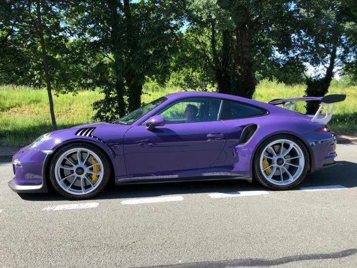 Porsche 991 GT3RS Ultra Violet  - Page 2 - Readers' Cars - PistonHeads - The image features a purple sports car parked on the side of a street. The car is positioned in such a way that its front end faces towards the camera, allowing us to see its design and features clearly. It appears to be an upscale model, possibly a limited-edition or special series vehicle, as suggested by its unique paint job and aftermarket parts. The car is equipped with large air intakes, a rear wing, and multiple exhaust pipes, all of which contribute to its sporty aesthetic.

The sports car is parked on the right side of the street, adjacent to a sidewalk where there are some trees. The surrounding environment suggests a residential or suburban area. There's a pedestrian crossing signal visible in the image, indicating that the vehicle is parked near an intersection. The image is clear and well-lit, allowing for a detailed view of the car and its immediate surroundings.