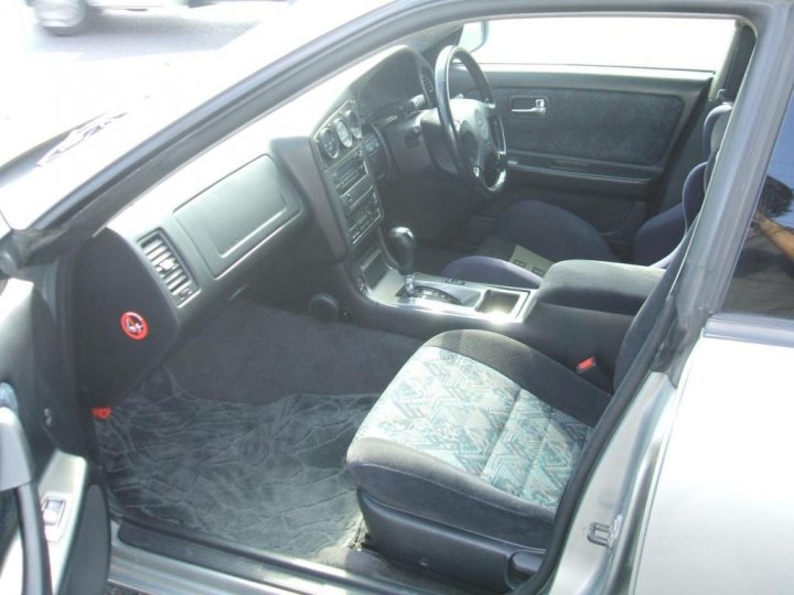 Sleeper Street Pistonheads - The image shows the interior of a car, focused on the passenger side. The scene includes the front seats, the dashboard with its controls and instruments, as well as the gear shift lever. The seats are upholstered in fabric, and the controls have a silver, metallic finish. There is a fabric-like substance scattered across the floor of the car, suggesting something may have been spilled or discarded. The lighting in the car suggests it is daytime with some natural light entering from the windows, causing the sunlight to reflect on the car's interior.