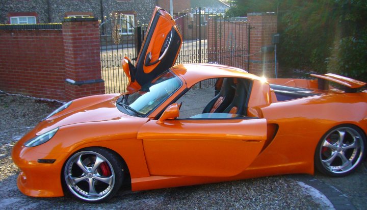 Yesterday Pistonheads Norwich - The image showcases a vibrant, meticulously maintained orange sports car parked on a gravel driveway. The car's doors are open, revealing the interior. The hood is propped up, displaying the engine. The vehicle also features dual exhaust pipes. Its positioning suggests it might be on display or waiting for an event.