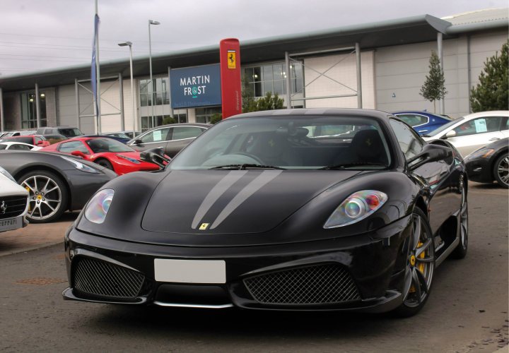 Scotland's Finest Spotted!! [Vol 2] - Page 323 - Scotland - PistonHeads - The image captures a scene at a car dealership. The main focus is a black sports car, featuring a distinctive yellow stripe and a distinctive sun-and-planets emblem on the grille. This car is displayed prominently in the foreground, suggesting it is the featured or sale vehicle.

In the background, several other cars are visible, indicating a variety of options available at the dealership. The dealership itself appears modern with a large, open layout that allows customers to walk around the displayed vehicles.

The number plate of the main car reads "101 KU3", and it is parked on a concrete lot. The sky is overcast, suggesting either early morning or late afternoon. Finally, the scene is set against the backdrop of the dealership's exterior, filled with signs and lights, indicating that it's an active business environment.

Overall, the image presents a snapshot of a diverse automobile sale atmosphere.