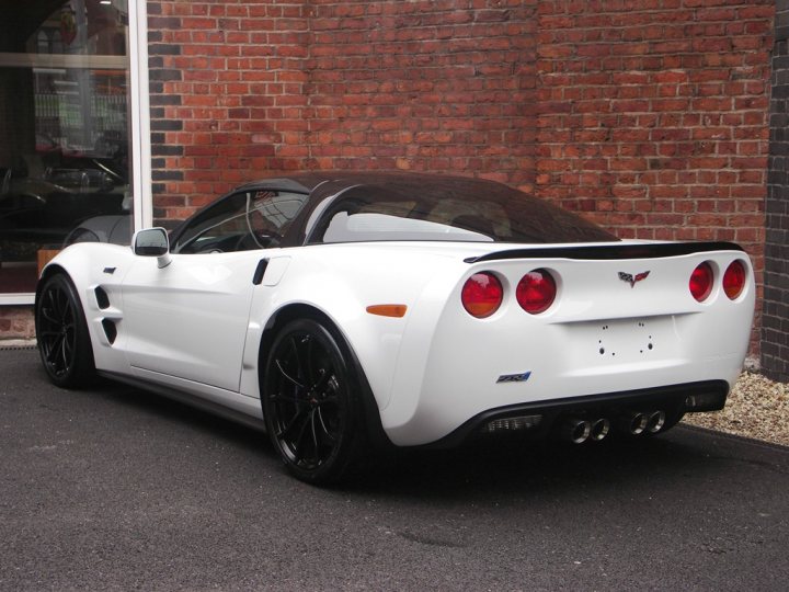 How about some ZR-1 photos to cheer you up? - Page 1 - Corvettes - PistonHeads - The image depicts a white Corvette convertible car parked outside a brick building. The car is sleek and modern with a black convertible roof, and it features red taillights. The Corvette is equipped with a spoiler, and there are visible exhaust pipes. The car is parked on a tarmac driveway.